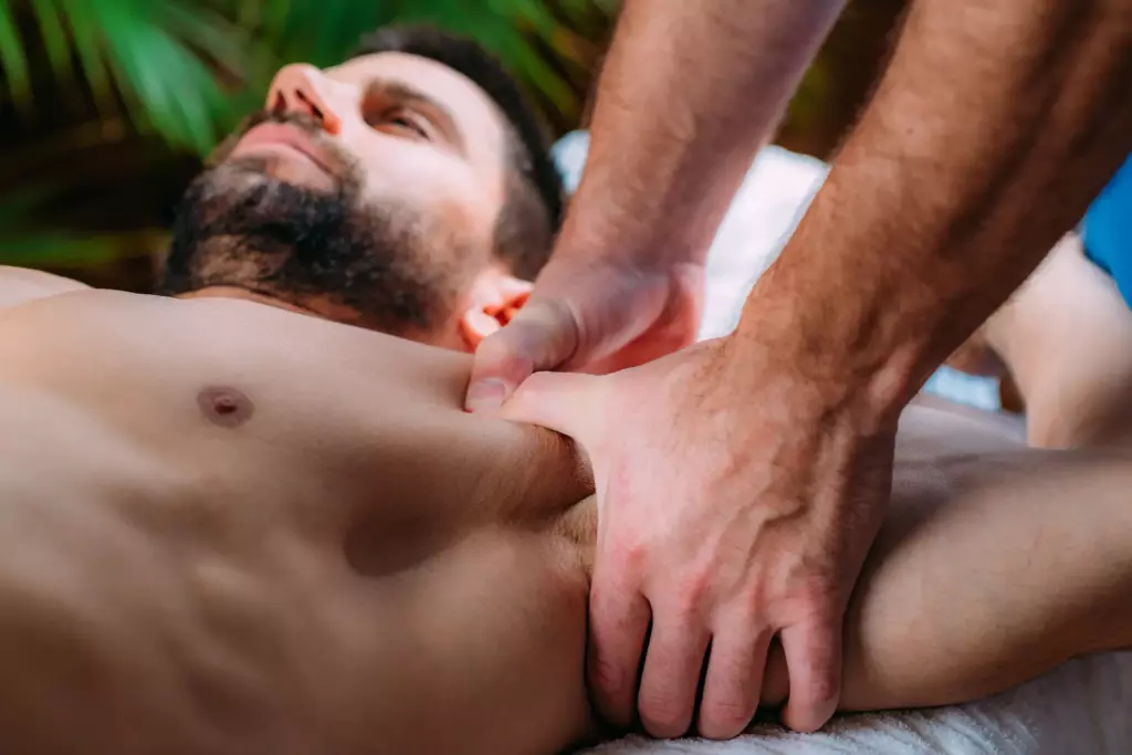Massage Therapy – A person receiving a deep tissue massage on their upper chest and shoulder area while lying down, with a therapist’s hands applying pressure. The background is blurred with green foliage visible. | Body Heal Therapy