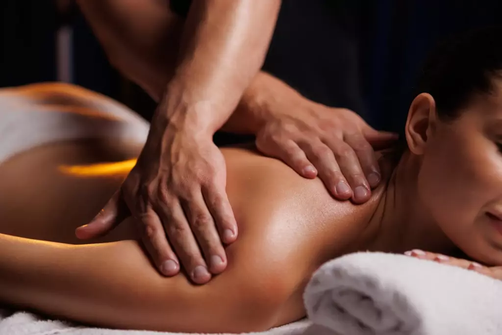 Massage Therapy – A person receives a back massage while lying face-down on a towel-covered table, with a relaxed expression and soft lighting creating a calm atmosphere. | Body Heal Therapy